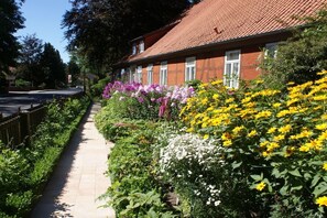 A residential building with a red-tiled roof, a paved pathway, and a variety of flowering plants. - Holiday apartment with 2 bedrooms (Neuenkirchen OT Delmsen)