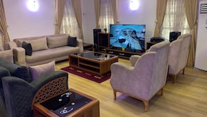 A living room with a sofa, armchairs, a coffee table, a TV, and a speaker system. - Raydee Apartment (Lugbe)