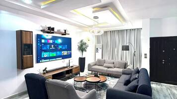 Un salon moderne avec un téléviseur à écran plat, des canapés, une table basse et une plante en pot.