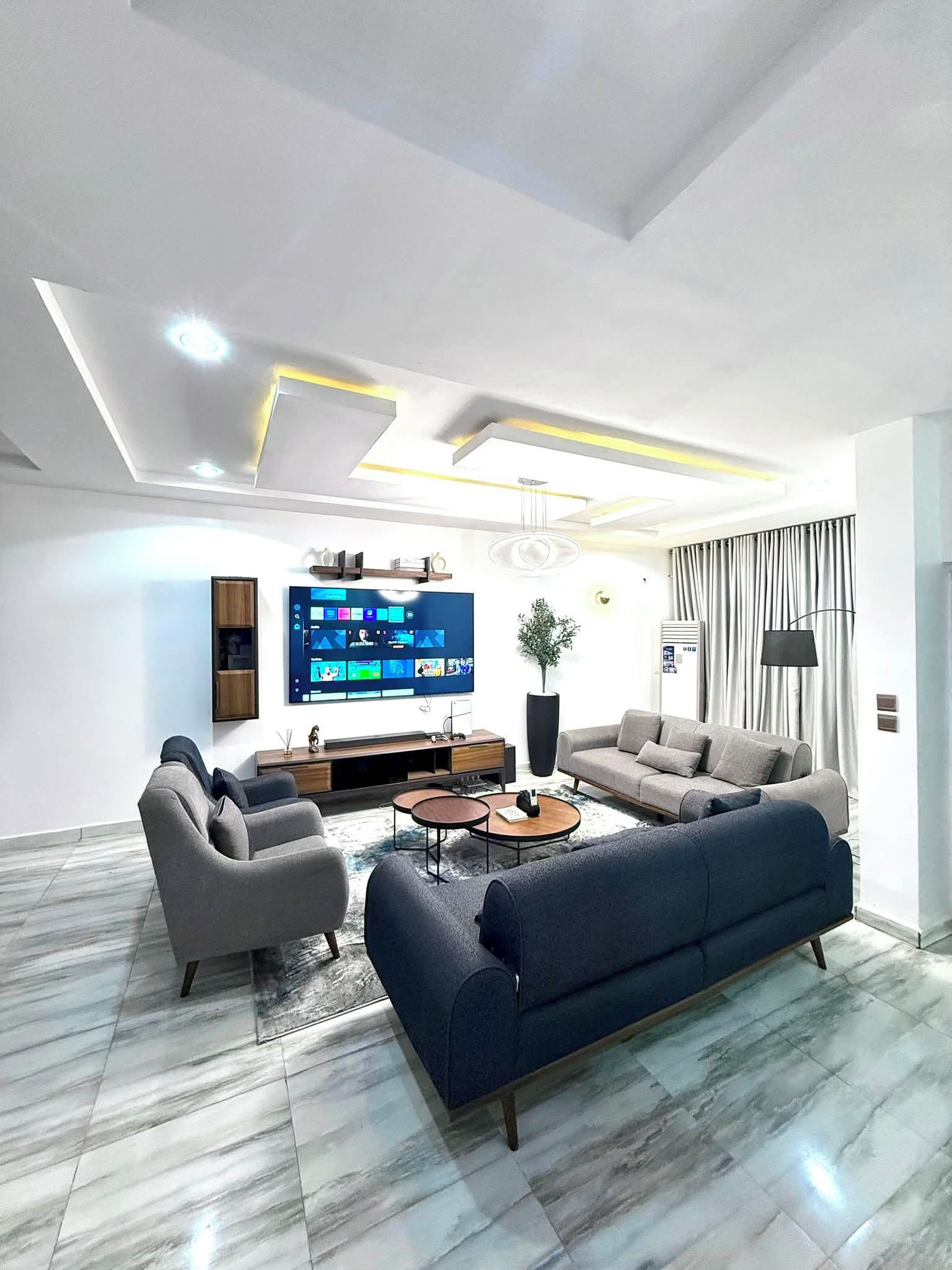Una sala de estar moderna con un televisor de pantalla plana grande, un sofá, dos sillones y una mesa de centro.