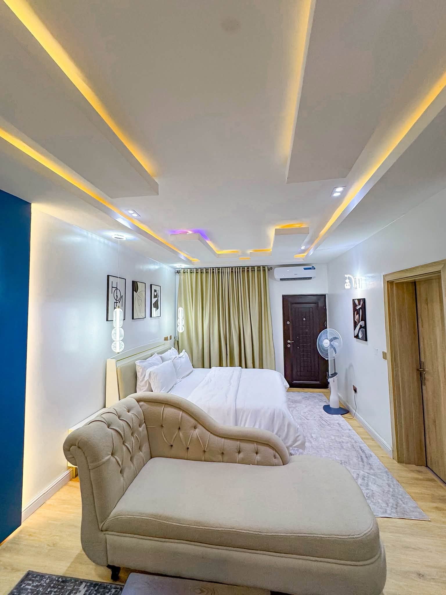 Ein modernes Schlafzimmer mit Bett, Sofa, Ventilator und einer Tür.