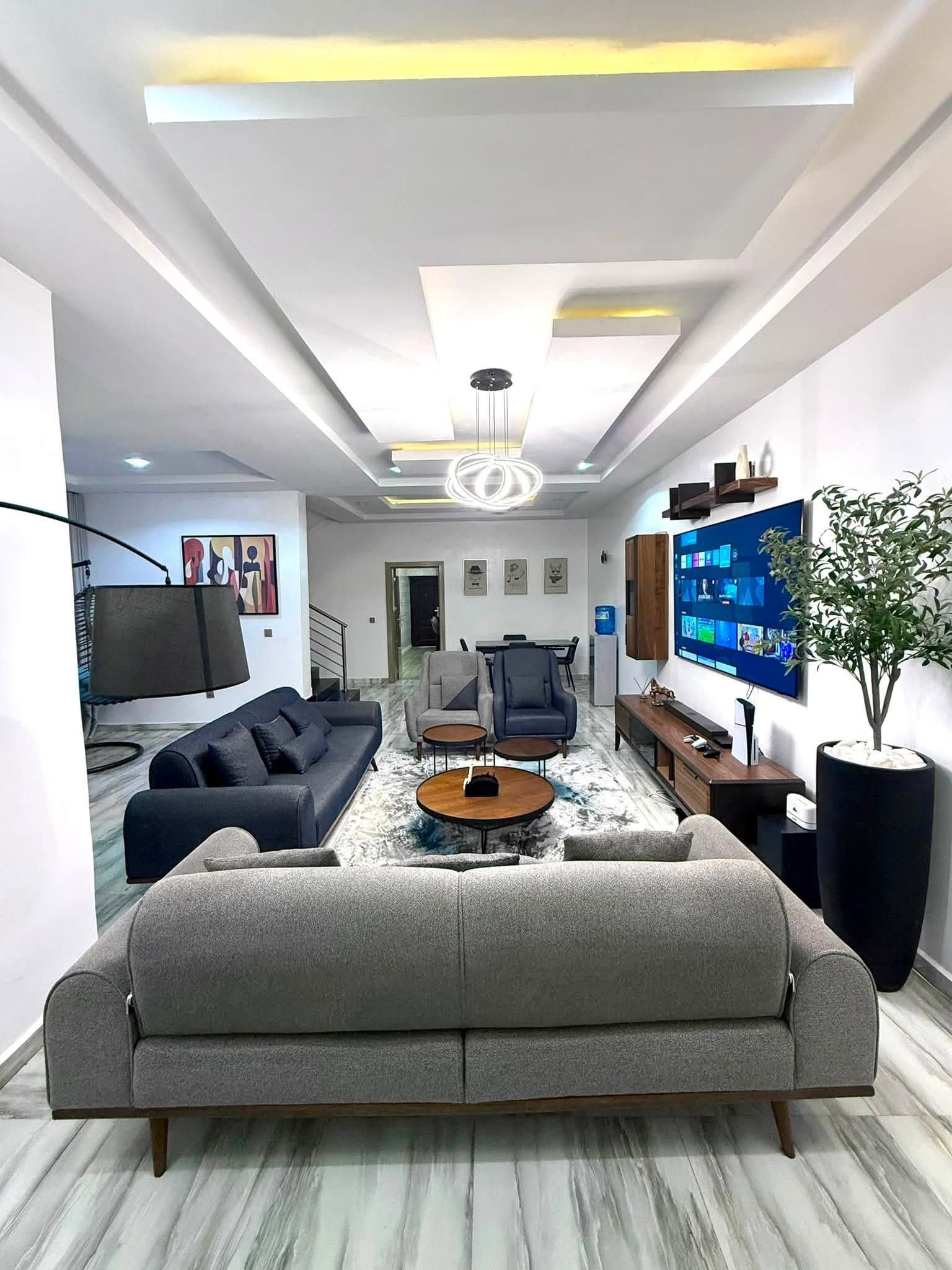 Ein modernes Wohnzimmer mit einer großen Couch, einem Couchtisch und einem flachbildfernseher, der an der Wand montiert ist.