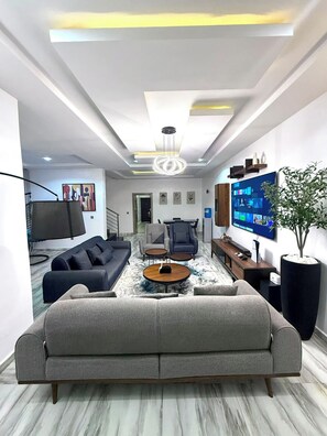 A modern living room with a sofa, coffee table, TV, and a large plant. - Raydee Apartment (Lugbe)