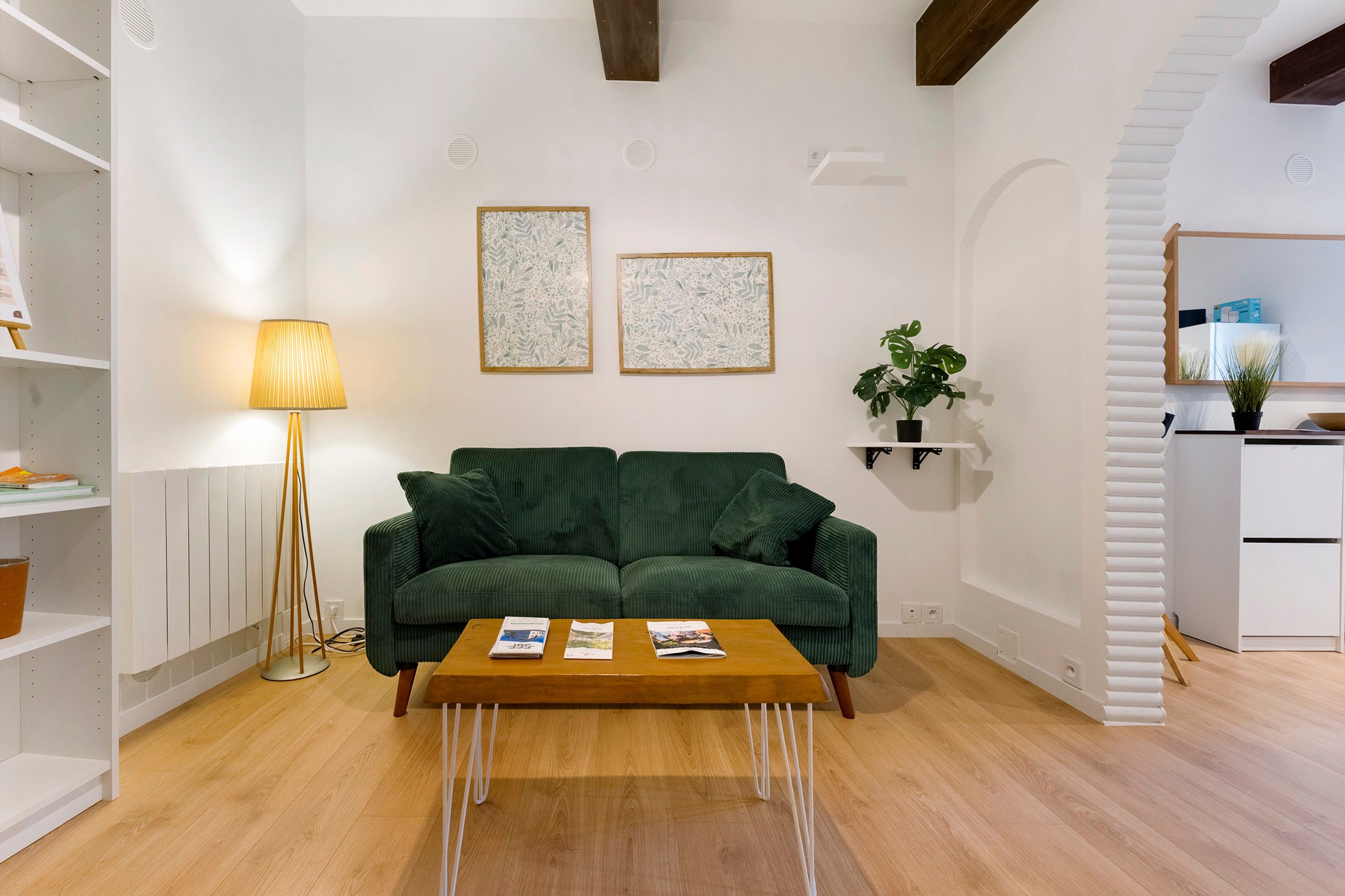 Un salon avec un canapé vert, une table basse en bois et deux œuvres d’art encadrées accrochées au mur.