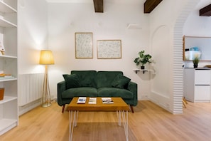 Un saló amb un sofà verd, una taula de centre de fusta i dos quadres amb marc a la paret.