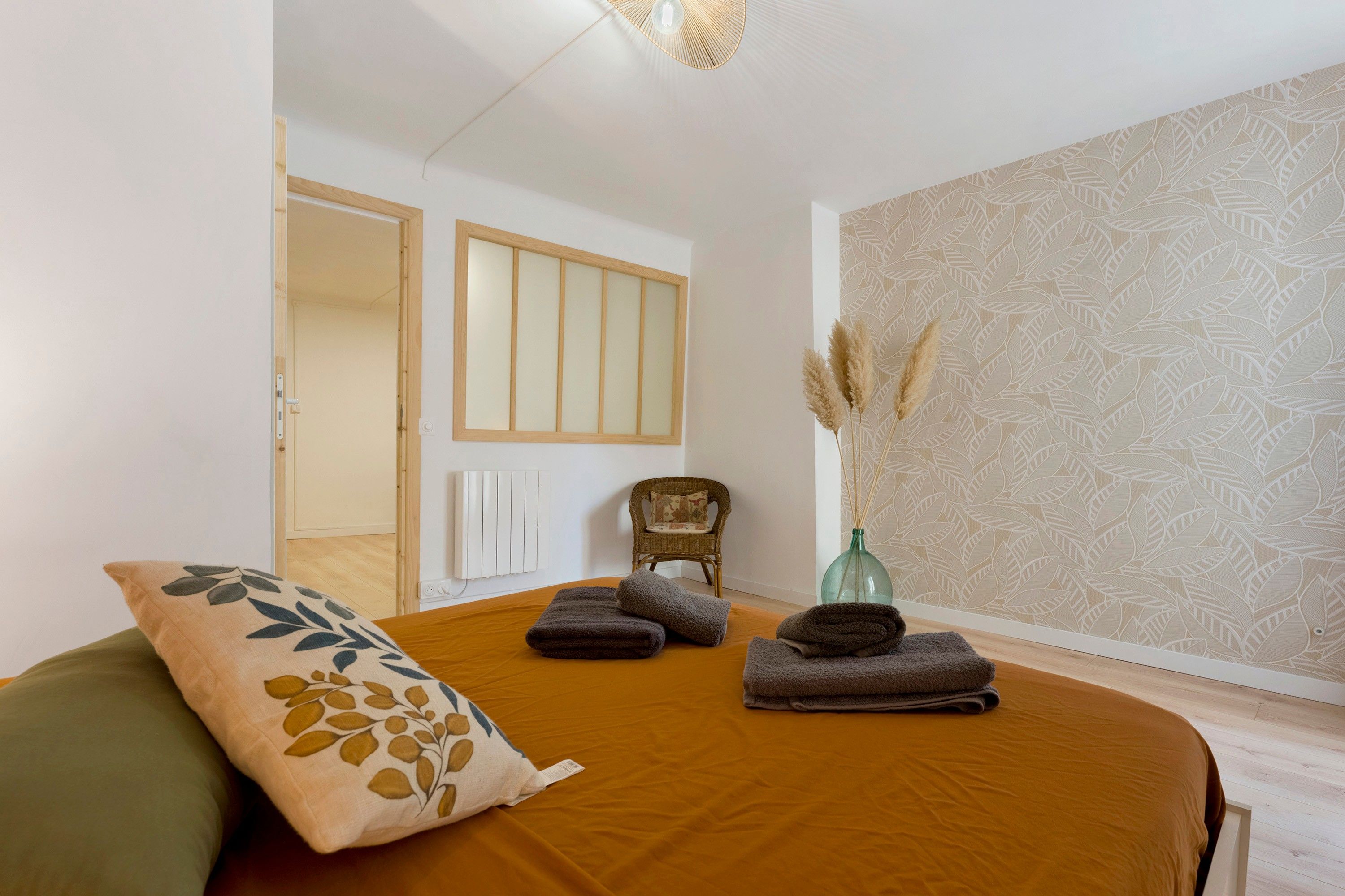 A bedroom with a bed, a chair, a radiator, and a wall with a leaf pattern.