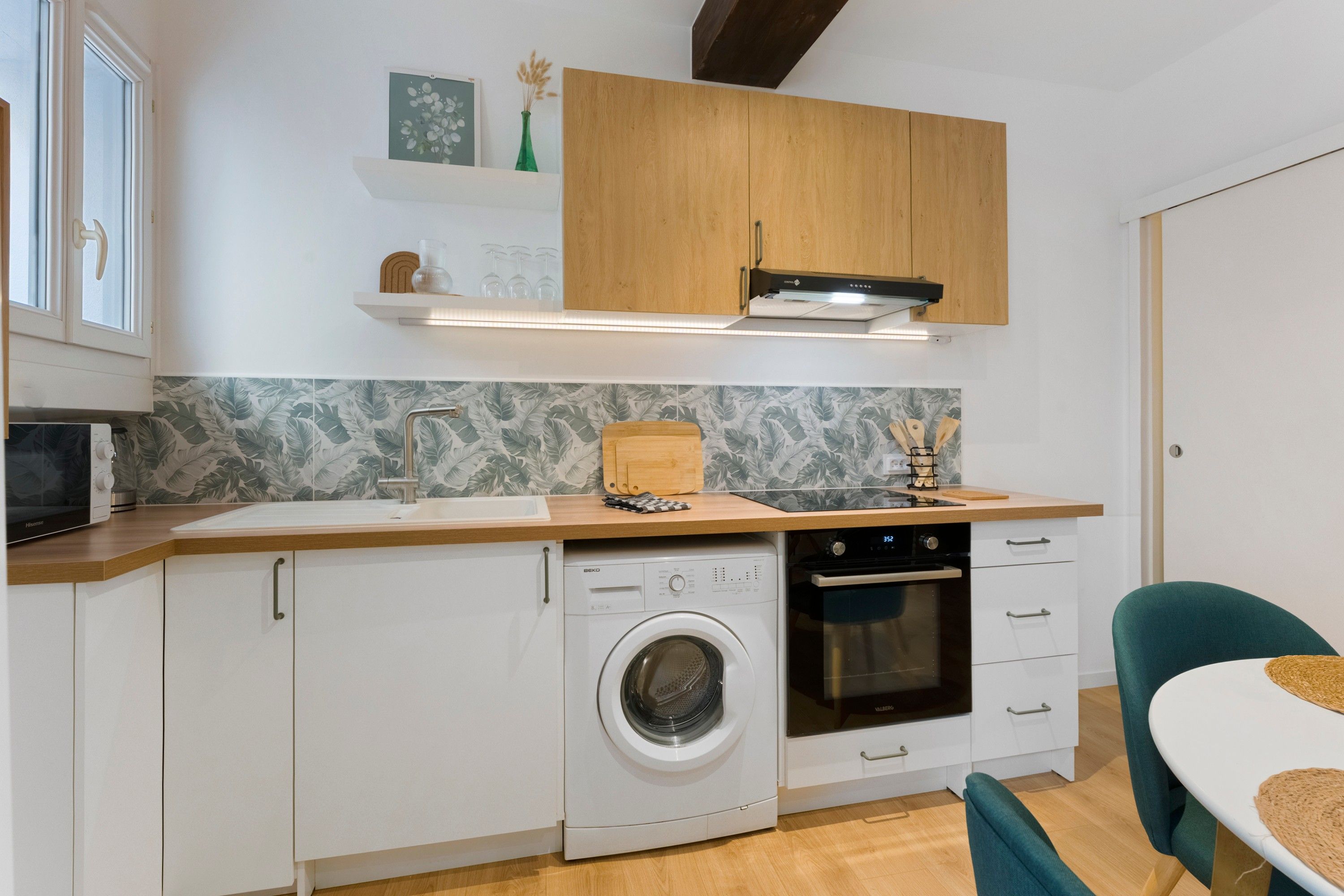 A compact kitchen with a washing machine, oven, and a dining area with a table and chairs.