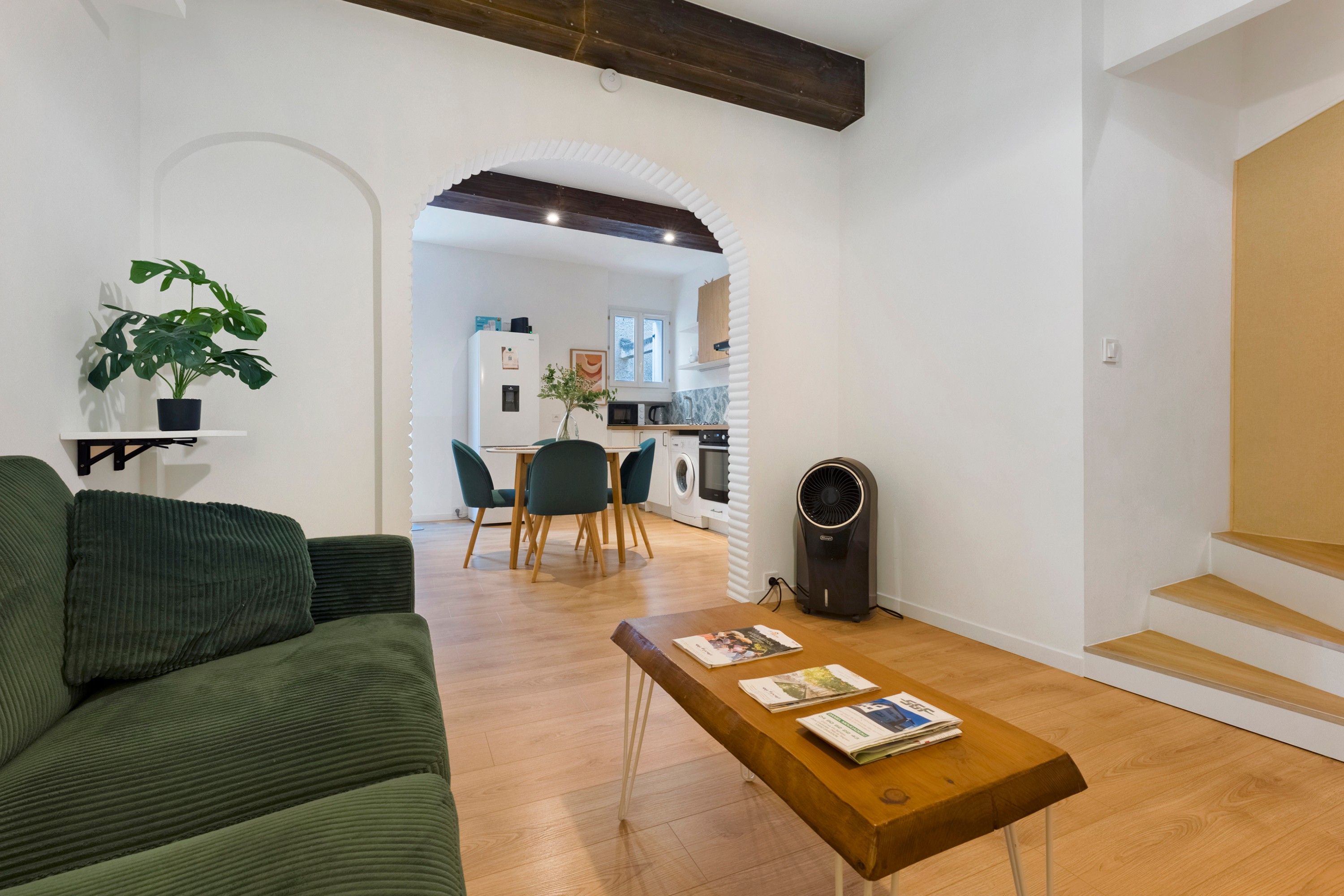 A modern living room with a green sofa, a wooden coffee table with magazines, and a potted plant.