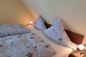 A bed with floral bedding and two pillows, a bedside lamp, and a nightstand with a lamp. - Holiday apartment in Juist with swimming pool (Juist)