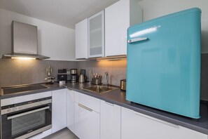 Une cuisine moderne dotée d’une hotte en acier inoxydable, d’un four encastré, d’un évier et d’un réfrigérateur de couleur turquoise.
