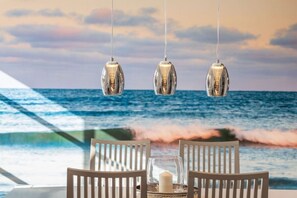 Ein Tisch mit Stühlen und einer Kerze, mit Blick auf das Meer und Wellen.