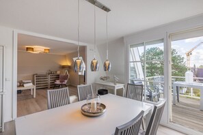Ein moderner Essbereich mit einem weißen Tisch, Stühlen und Pendelleuchten.