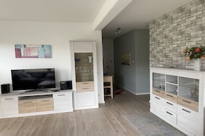A modern living room with a flat-screen TV, a white entertainment unit, and a brick accent wall. - Holiday apartment with 1 bedroom (Scharbeutz)