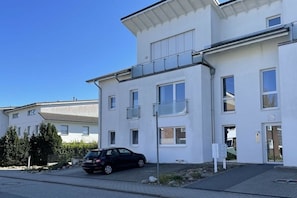 A modern building with a car parked in front, a clear sky, and a well-maintained lawn. - Holiday apartment with 1 bedroom (Scharbeutz)