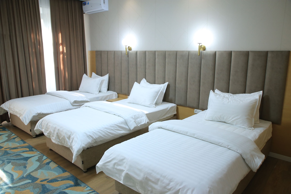 A hotel room with three single beds, a large padded headboard, and a patterned carpet.