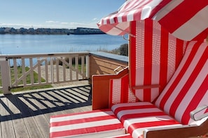 A deck with a red and white striped lounge chair and a view of the water. - At the Baltic Sea Resort Olpenitz marina (Kappeln)