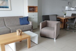 Ein modernes Wohnzimmer mit einer Couch, einem Couchtisch und einem Sessel. Es gibt eine Essecke mit Tisch und Stühlen.