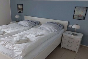 Un lit double avec du linge de lit blanc et des oreillers à rayures, deux tables de chevet avec des lampes, et deux tableaux encadrés accrochés aux murs.