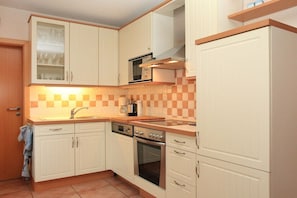 Cuina amb armaris blancs, microones, forn i salabost a la paret.
