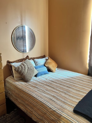 A neatly made bed with a striped bedspread, a round mirror on the wall, and a wooden headboard. -     Charming 2BR Baltimore Retreat Near Johns Hopkins (Baltimore)
