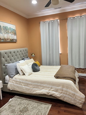 Ein Schlafzimmer mit einer gebügelten Kopfstütze, einem Bett mit gestreifter Bettdecke, mehreren Kissen, einem Nachttisch, einer Lampe und einem Bild an der Wand.