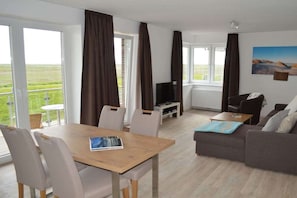 Ein modernes Wohnzimmer mit Essbereich, großen Fenstern, einem Flachbildfernseher und einer Couch.