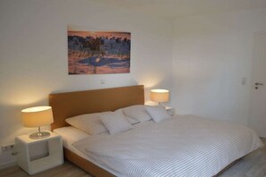 Ein Schlafzimmer mit einem Bett, zwei Nachttischlampen, einem Nachttisch und einem Wandbild.
