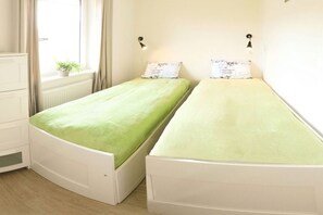 A room with two single beds, a dresser, and a window with curtains. - Holiday apartment with 1 bedroom (Fehmarn OT Burg)