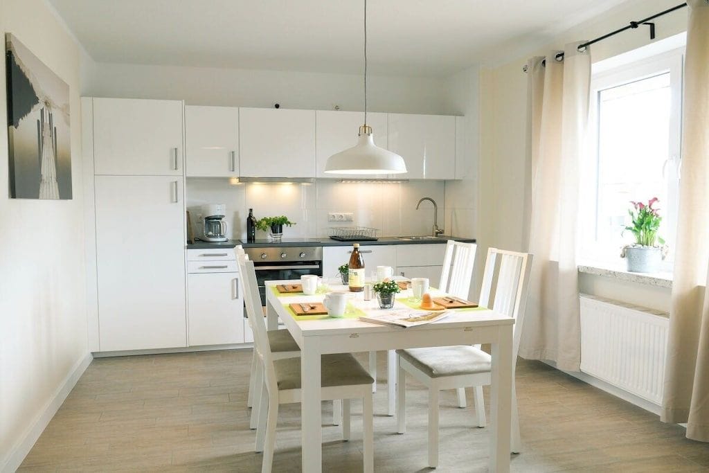 A modern kitchen with white cabinetry, a dining table set for four, and a pendant light.