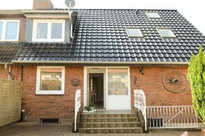 A two-story house with a tiled roof, a front door, and a small porch with steps. - Holiday apartment with 1 bedroom (Fehmarn OT Burg)