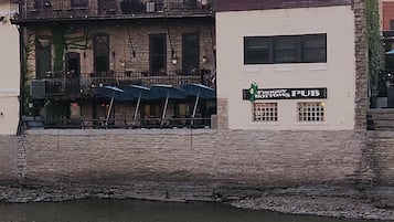 A waterfront building with a pub sign, multiple windows, and outdoor seating with umbrellas.