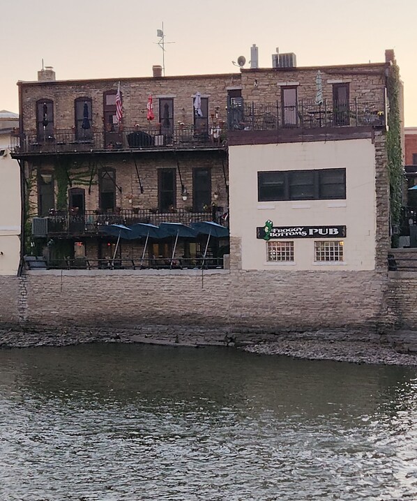A waterfront building with a pub sign, multiple windows, and outdoor seating with umbrellas.