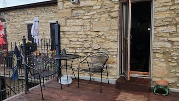 A stone building with a wooden deck, outdoor seating, and a door leading inside.