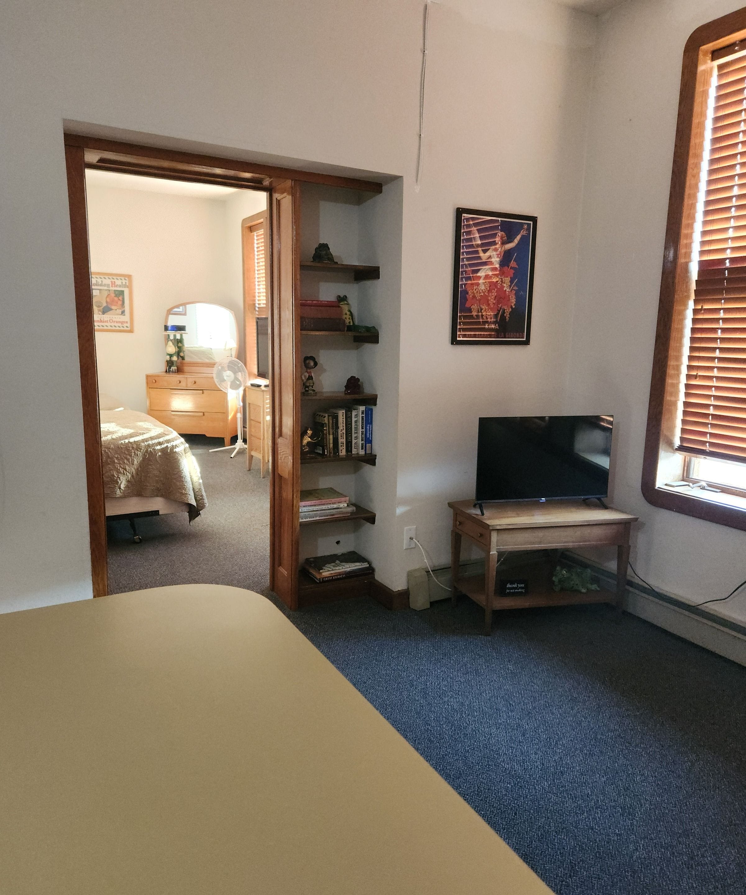 Un dormitorio con cama, televisor, estantería y puerta que da a otra habitación.