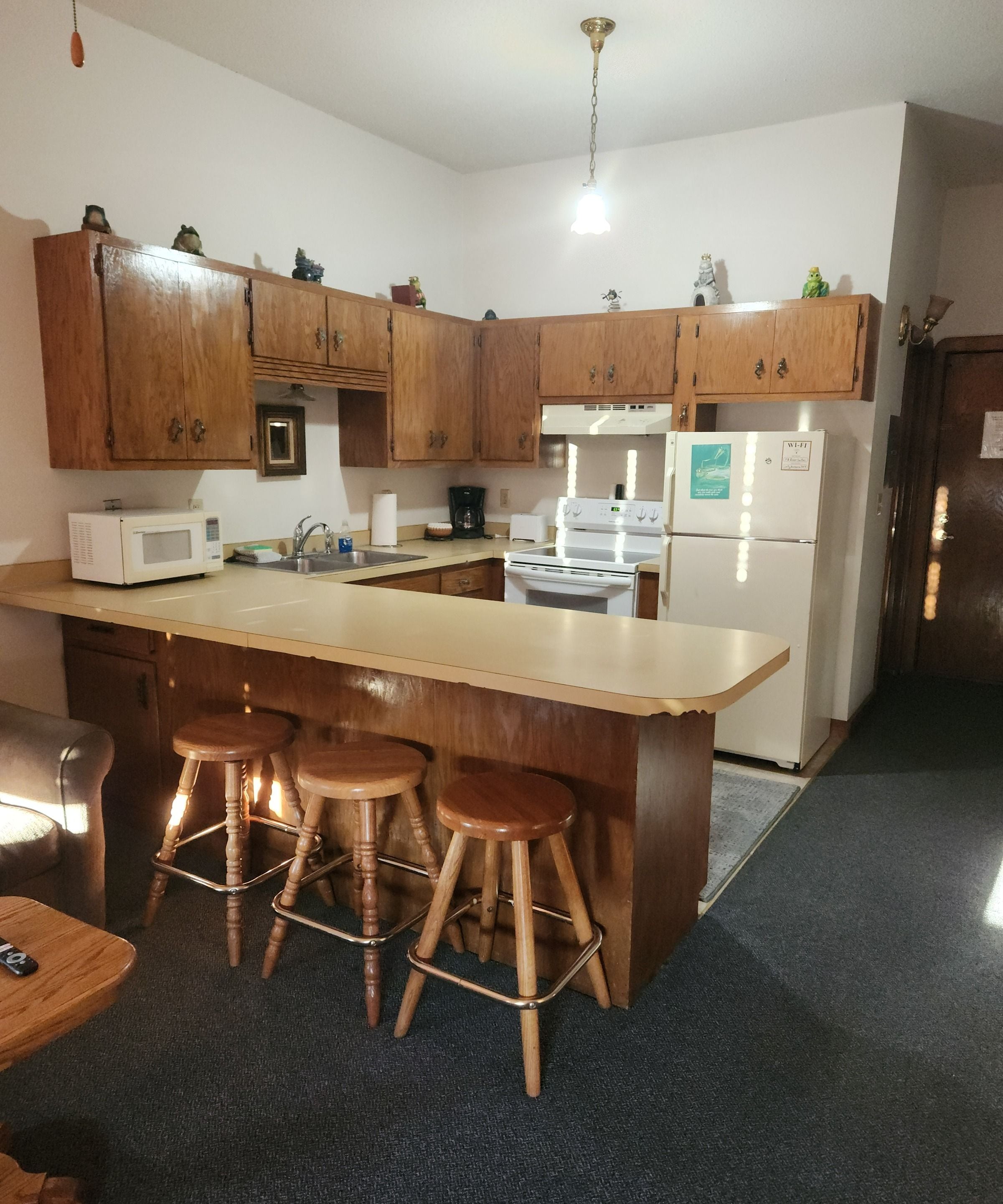 Une cuisine avec des armoires en bois, un four à micro-ondes, une cuisinière et un réfrigérateur. Il y a trois tabourets en bois près de l’îlot central.