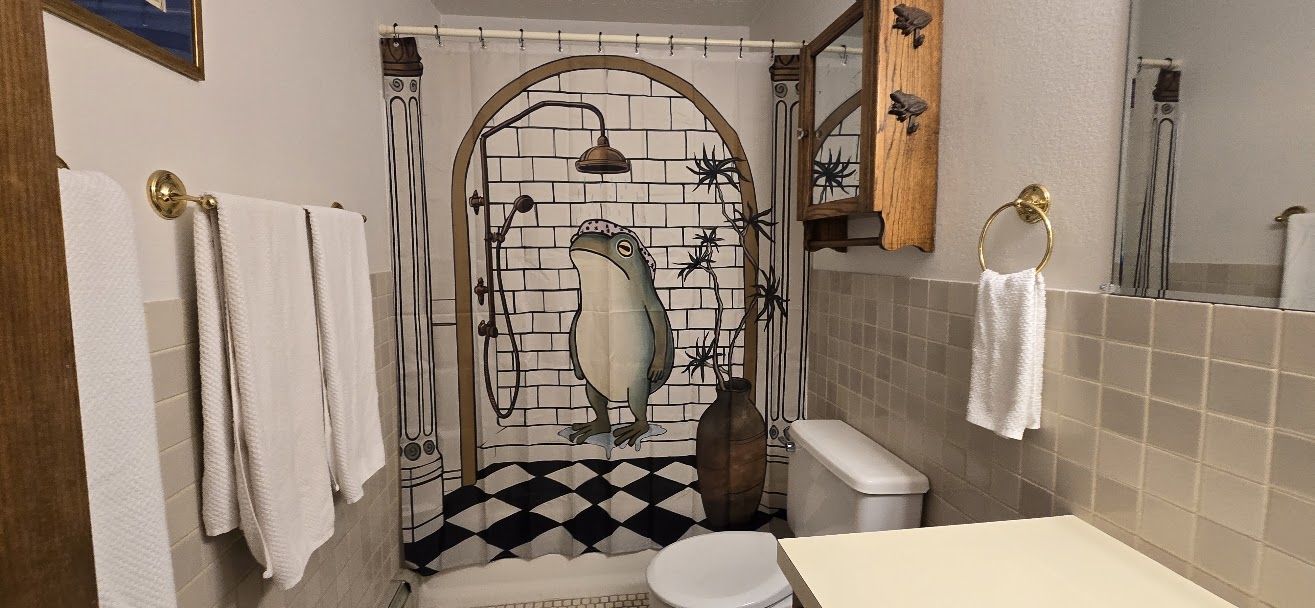 A bathroom with a shower, toilet, and a decorative frog mural.