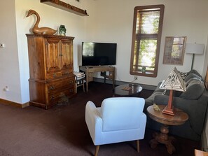 Una sala de estar con un mueble de madera, un televisor, un sofá y un sillón estampado.