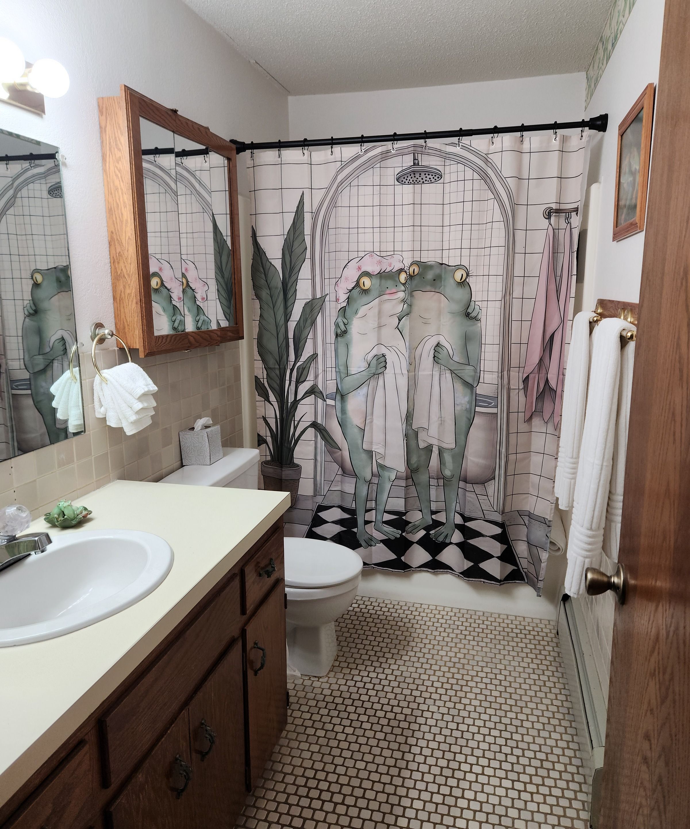 A bathroom with a sink, mirror, toilet, and shower curtain with a frog design.