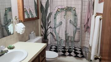 A bathroom with a sink, mirror, toilet, and shower curtain with a frog design.