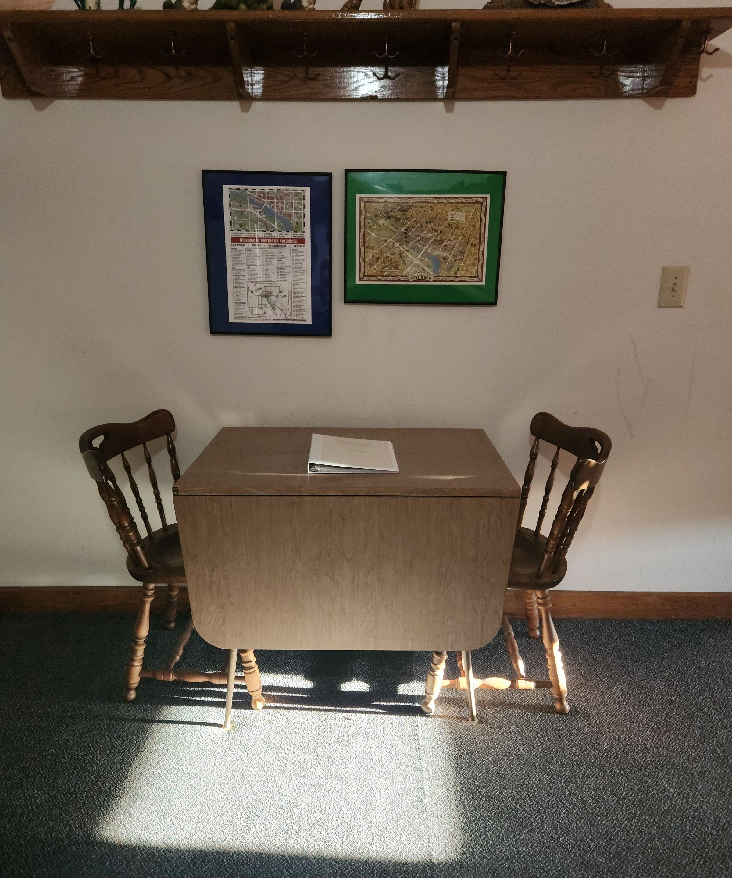 A room with a table and two chairs, a framed map on the wall, and a light switch.