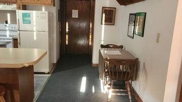 Cozinha com geladeira, fogão e armários de madeira. Há uma mesa de jantar com cadeiras e uma prateleira fixada na parede acima.