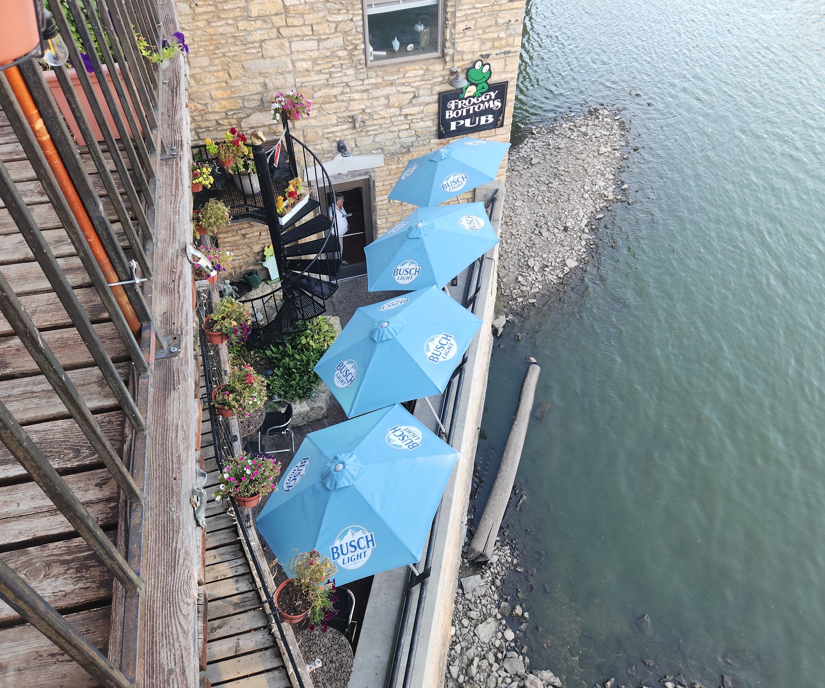 Terrasse extérieure avec des parasols bleus, un bâtiment en pierre et une enseigne indiquant « Froggy Bottoms Pub ».