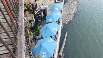 Terrasse extérieure avec des parasols bleus, un bâtiment en pierre et une enseigne indiquant « Froggy Bottoms Pub ».
