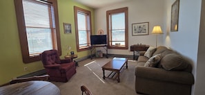 A living room with a TV, two windows, a sofa, a chair, and a lamp.