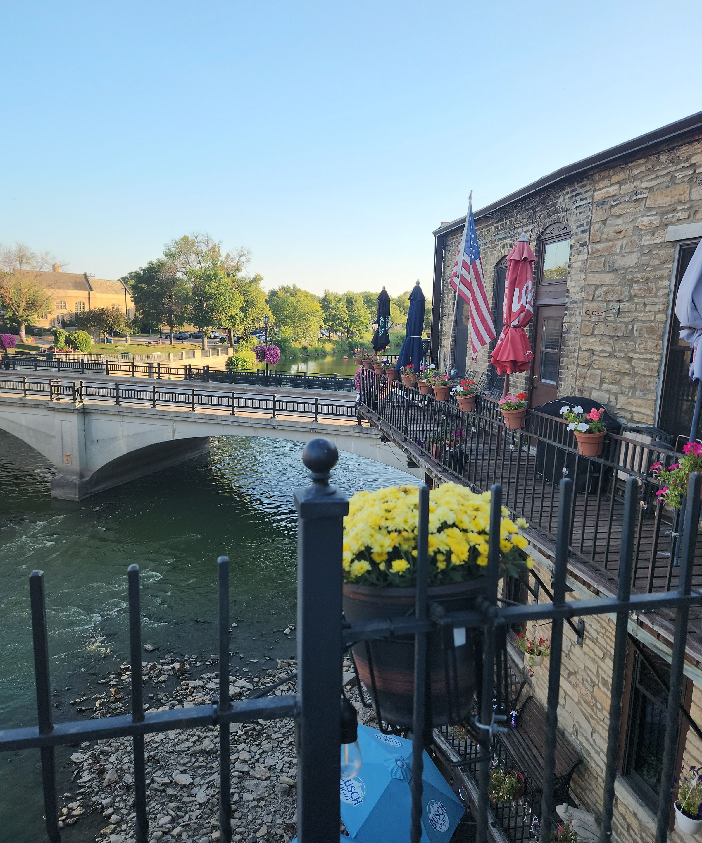 A riverside view with a stone building, a bridge, and potted flowers.