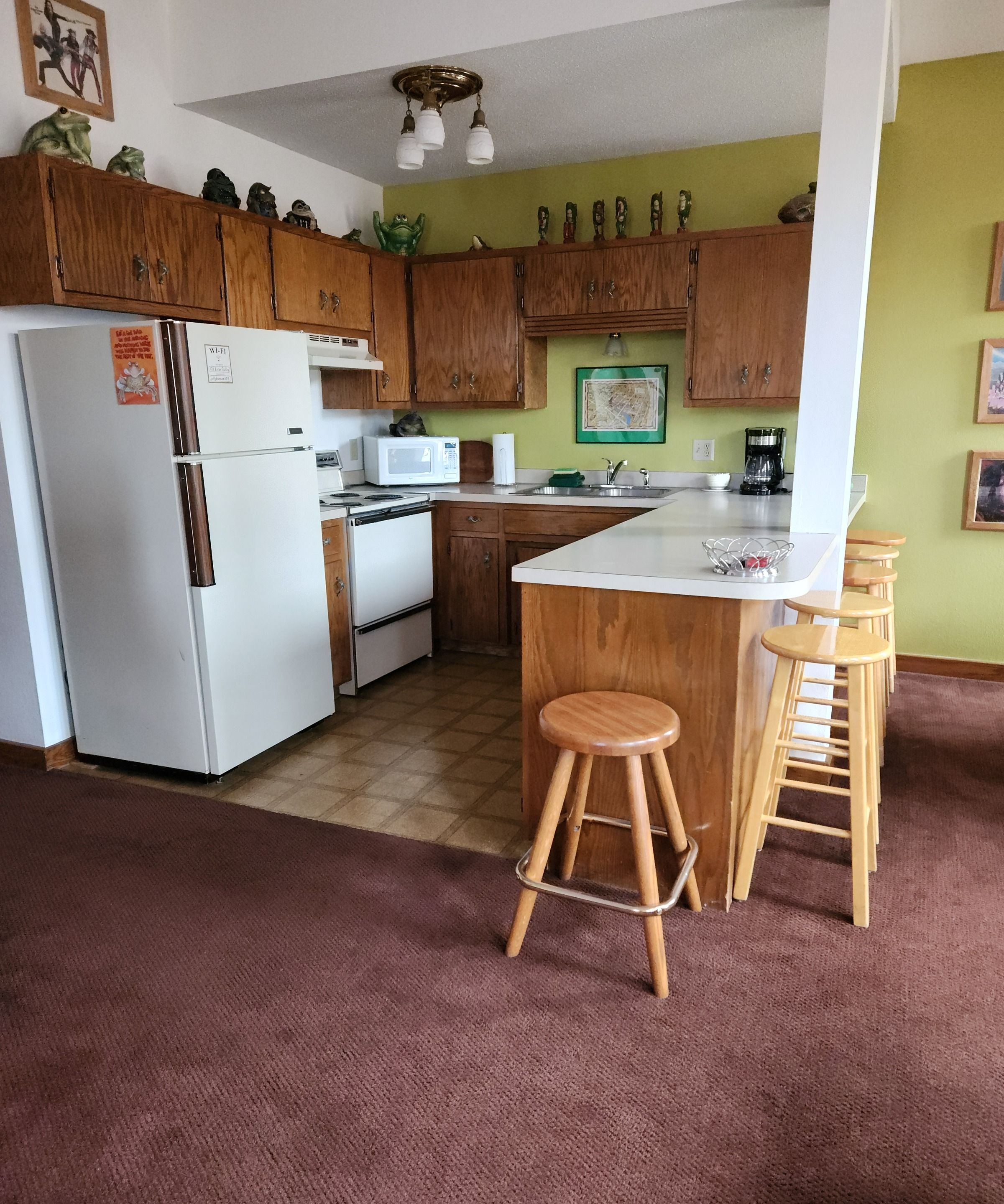 A kitchen with wooden cabinets, a refrigerator, a microwave, a stove, and a bar area with stools.