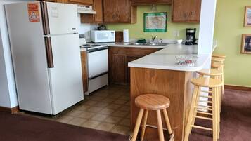 A kitchen with wooden cabinets, a refrigerator, a microwave, a stove, and a bar area with stools.