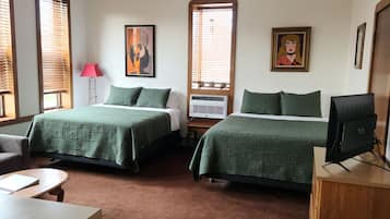 A hotel room with two beds, a desk, a chair, a desk lamp, and a television.