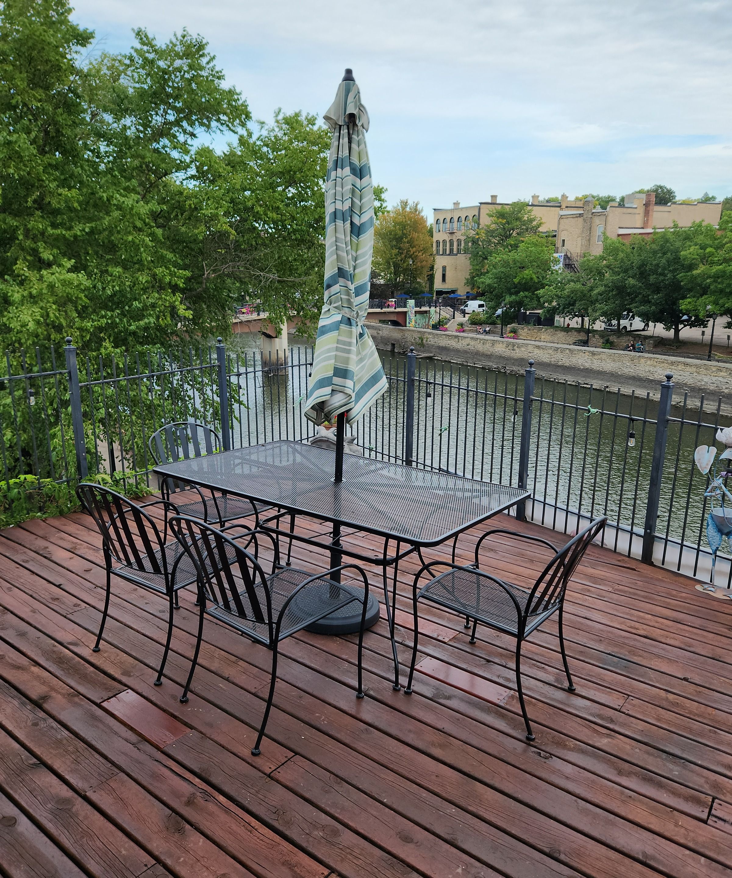 A deck with a table and chairs, overlooking a river with a fence and trees.