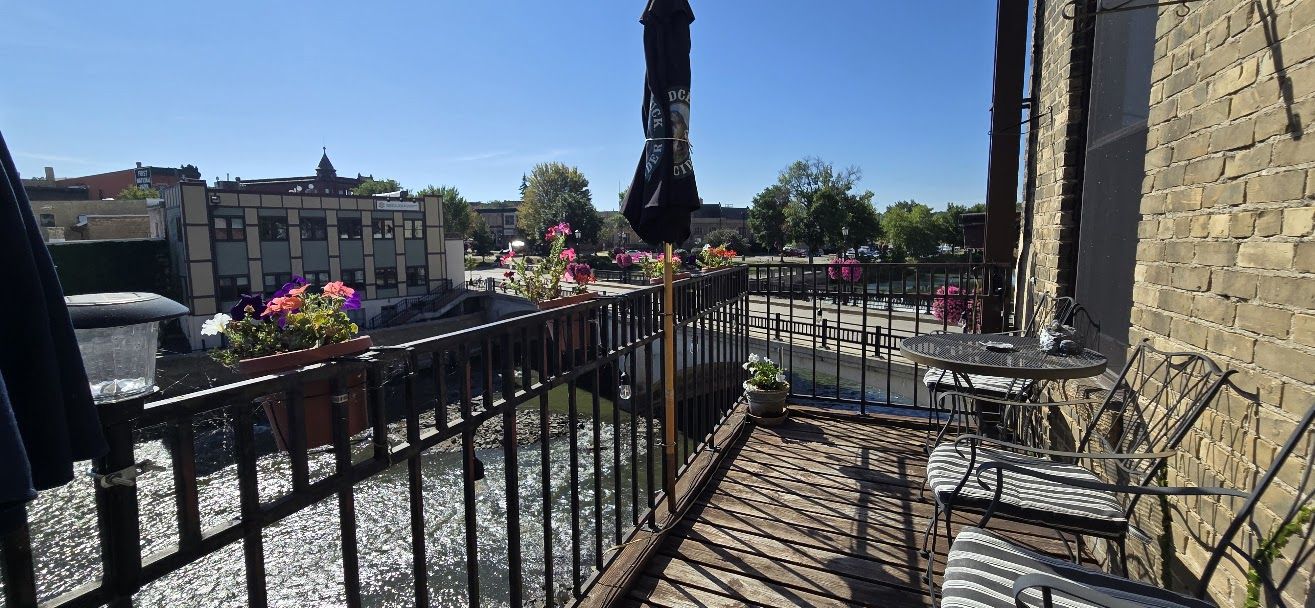 A balcony with a metal railing, potted plants, and a table with chairs.
